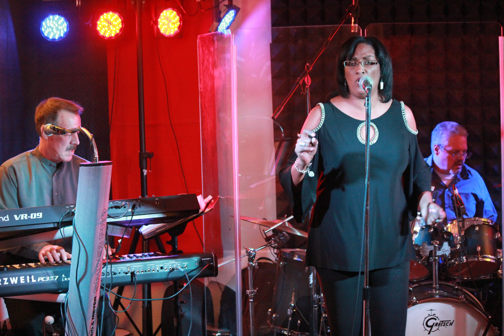 A live music performance featuring a singer with a microphone and a keyboard player, illuminated by colored stage lights.